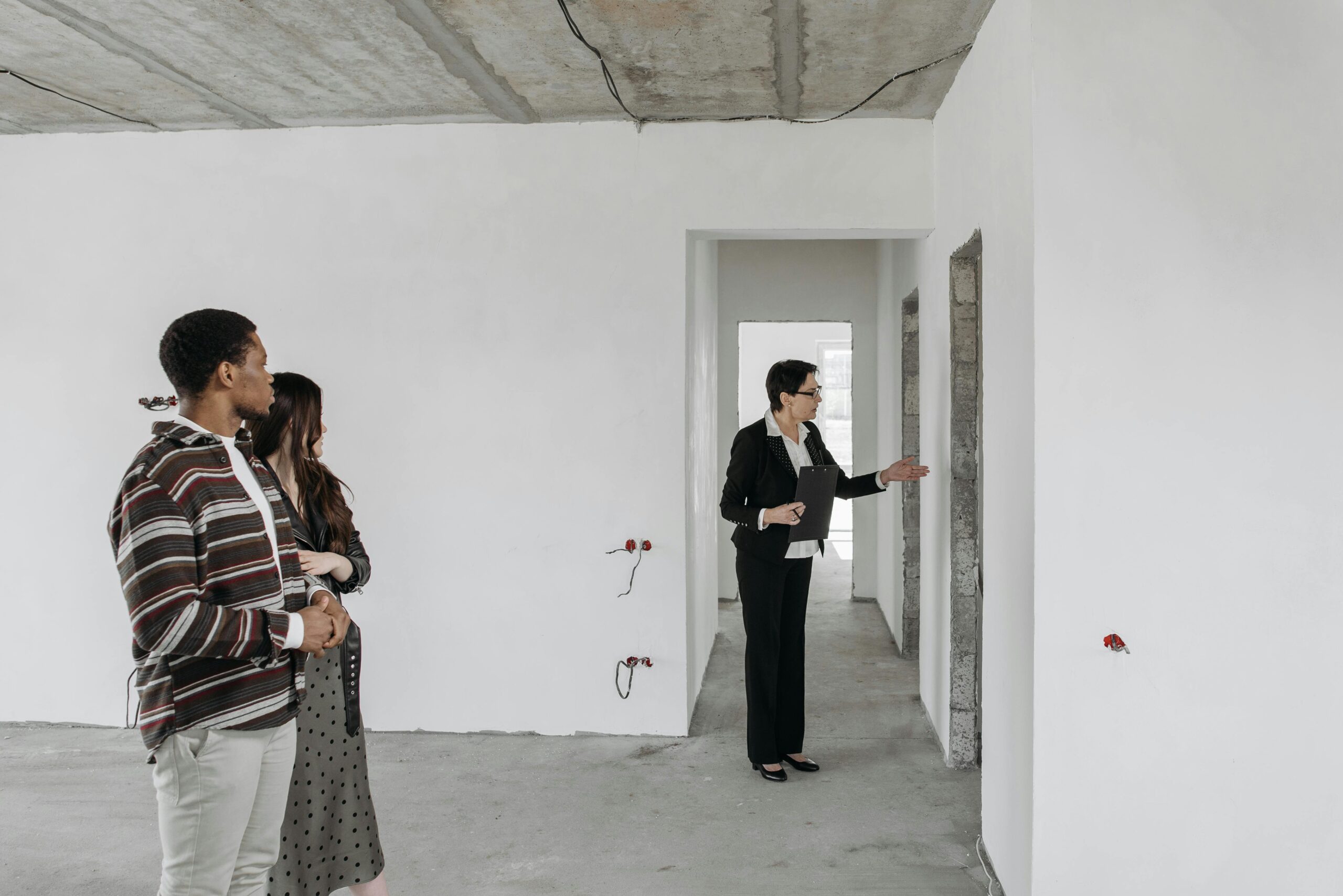 A couple explores an unfinished apartment with a real estate agent, considering property purchase options.